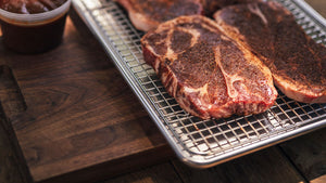 Pork steaks resting on a half sheet pan and wire rack before grilling.